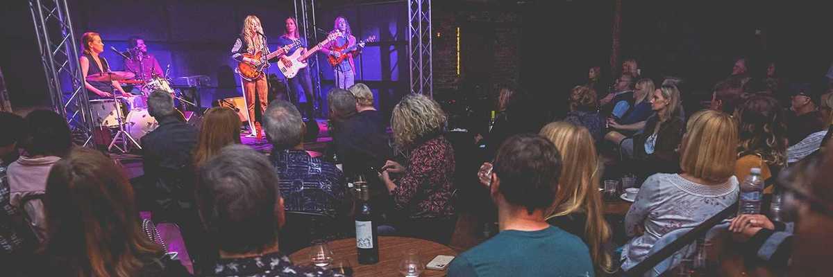 a band on stage and a room full of people watching them with wine
