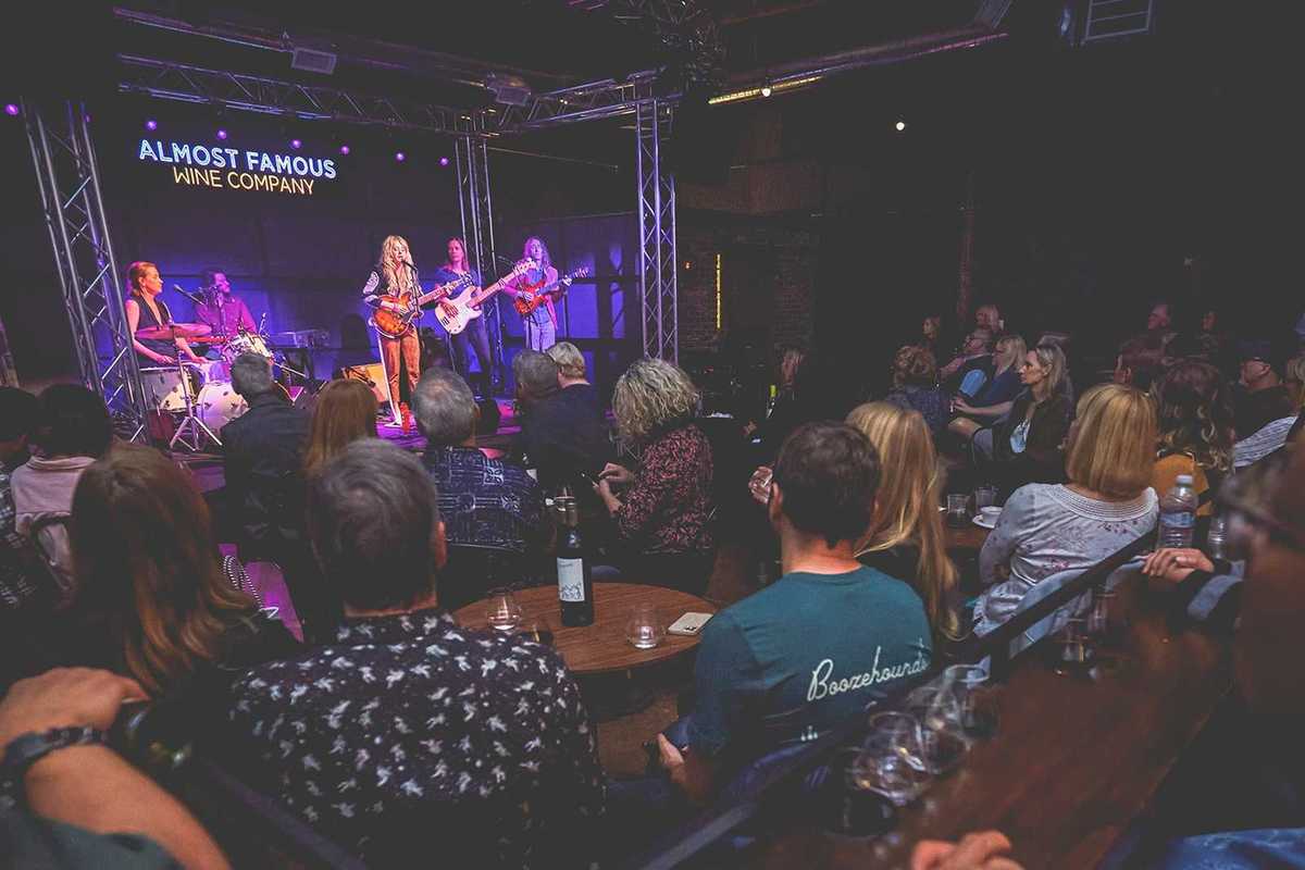 a band on stage and a room full of people watching them with wine