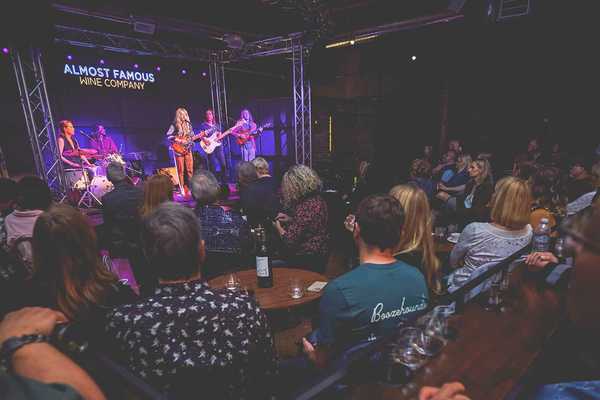 a band on stage and a room full of people watching them with wine