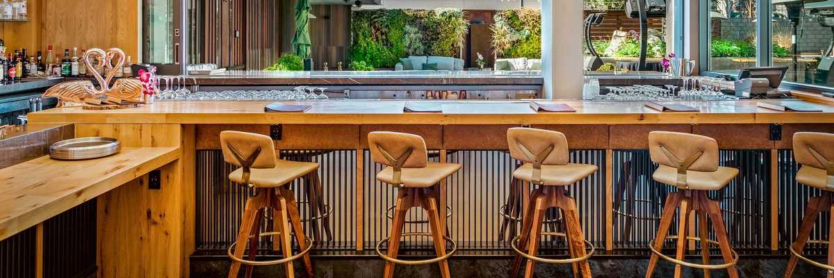 a bar with wooden stools with backs and hanging lights and a large open window