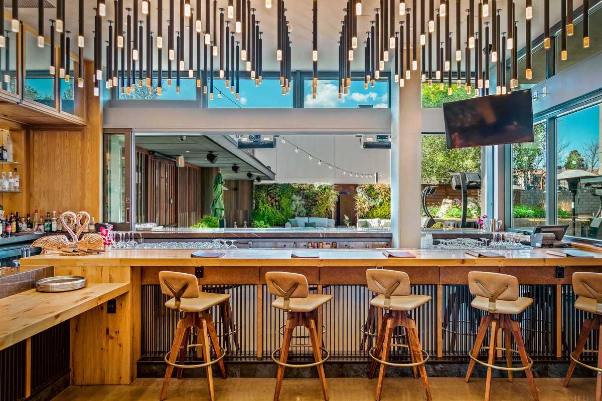 a bar with wooden stools with backs and hanging lights and a large open window