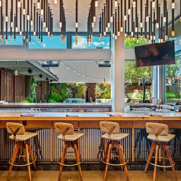 a bar with wooden stools with backs and hanging lights and a large open window