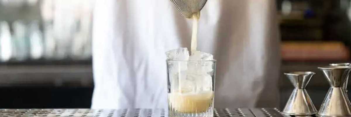 a bartender pouring a drink from a cocktail shaker through a sieve into a glass
