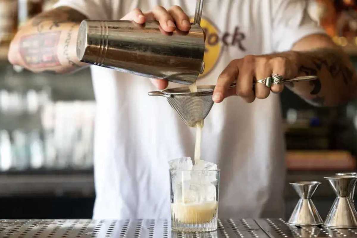 a bartender pouring a drink from a cocktail shaker through a sieve into a glass