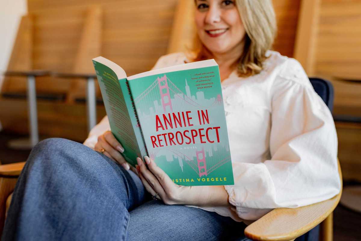 a blonde woman in a white shirt holding the book 'Annie In Retrospect'