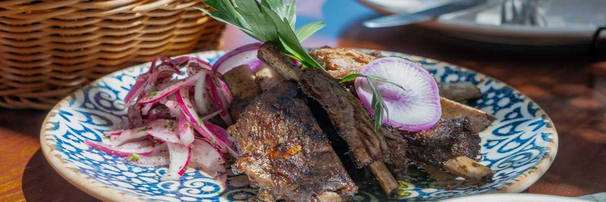 a blue decorated plate with grilled meat and onions on a table with a basket of bread