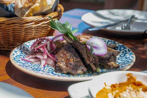 a blue decorated plate with grilled meat and onions on a table with a basket of bread