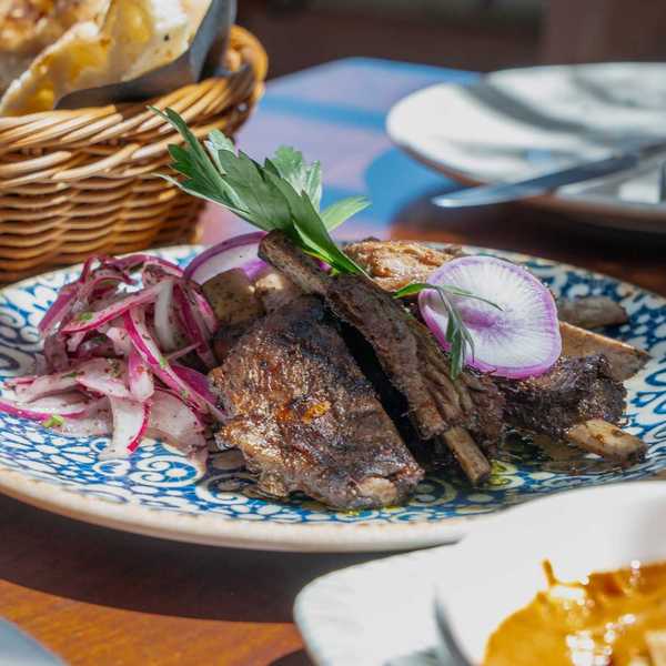 a blue decorated plate with grilled meat and onions on a table with a basket of bread