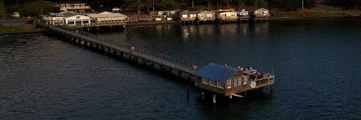 a boathouse on a pier in the middle of water with a set of buildings against the shore
