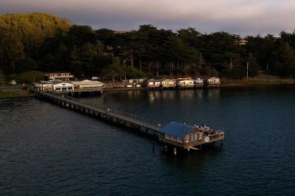 a boathouse on a pier in the middle of water with a set of buildings against the shore