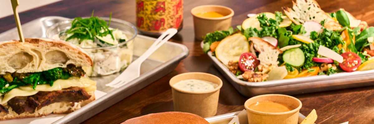 a burger, a meaty sandwich , and a salad plus sauces and fries on a table
