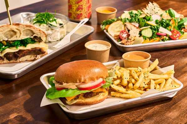 a burger, a meaty sandwich , and a salad plus sauces and fries on a table