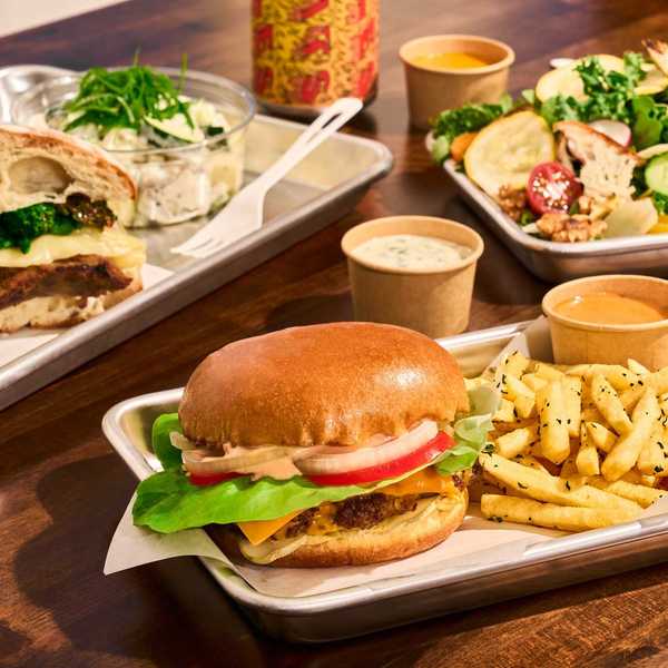a burger, a meaty sandwich , and a salad plus sauces and fries on a table