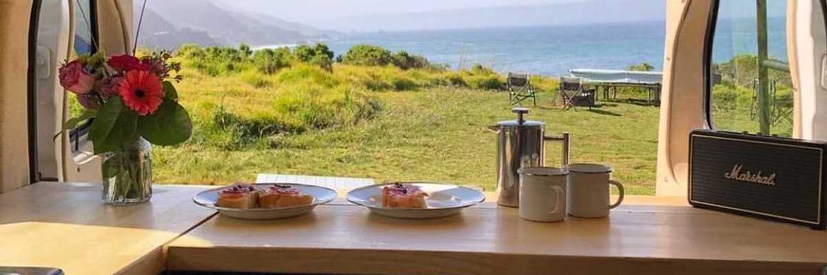a camper van with the doors open to the ocean and a campsite on the bluff