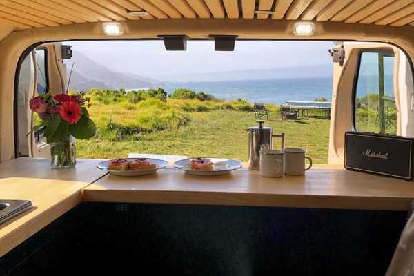 a camper van with the doors open to the ocean and a campsite on the bluff