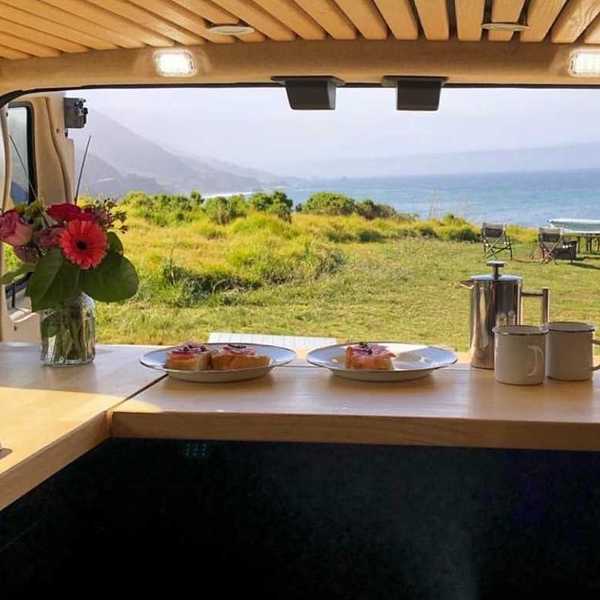 a camper van with the doors open to the ocean and a campsite on the bluff