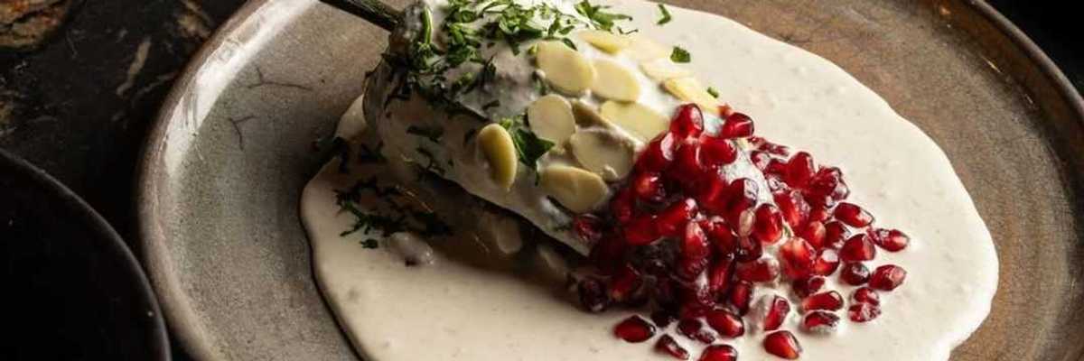 a chile in white sauce with pepitas on the upper half and pomegranate seeds on the lower