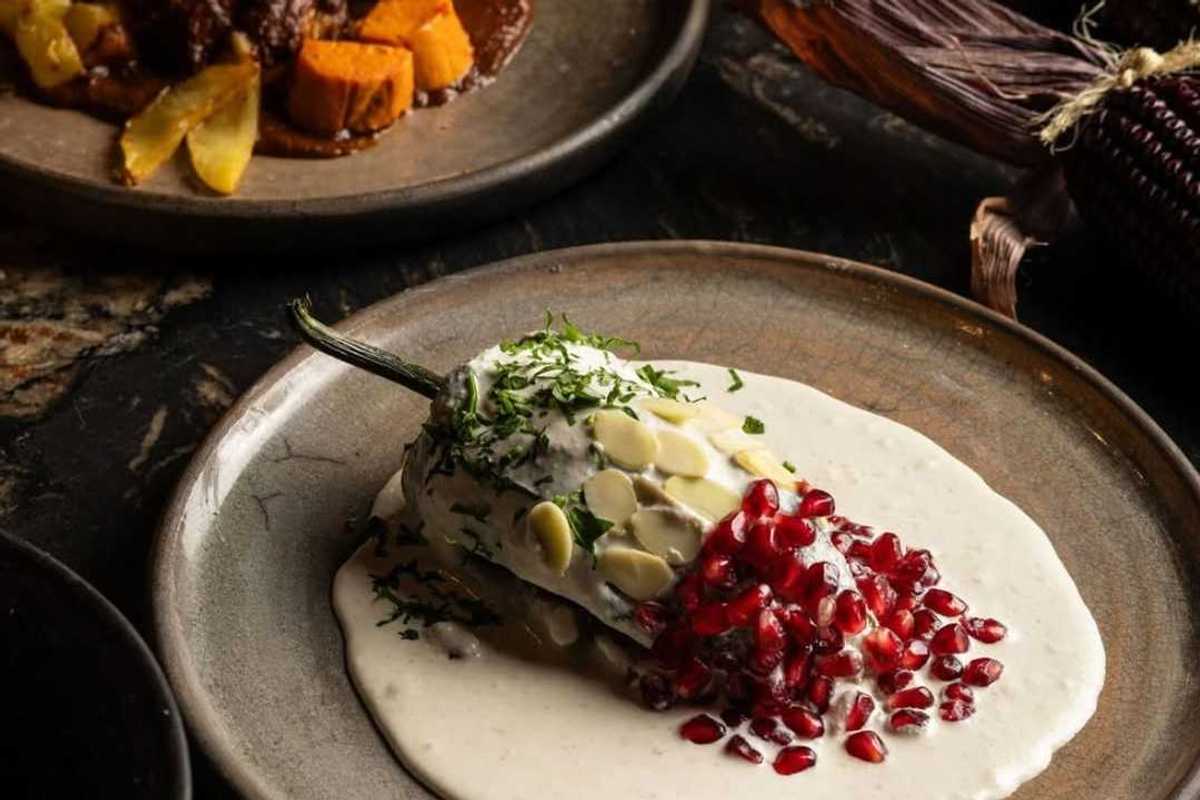 a chile in white sauce with pepitas on the upper half and pomegranate seeds on the lower
