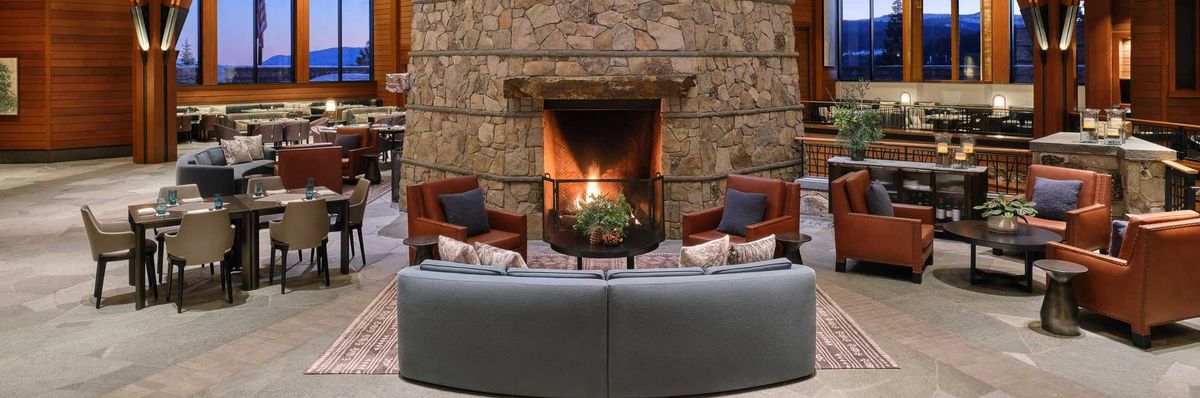 a cozy lounge with a large stone fireplace, wood beams, and lots of seating