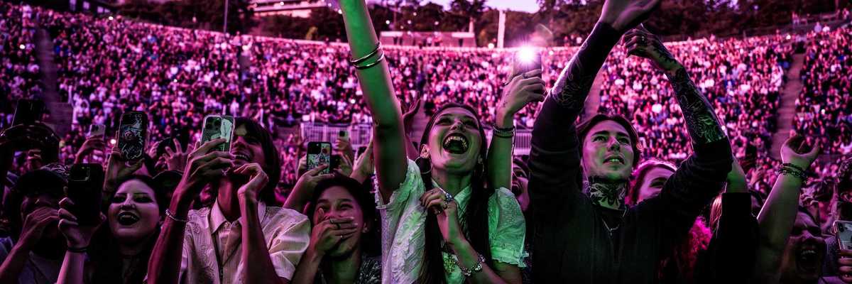 a crowd of outdoor concert goers bathed in pink light