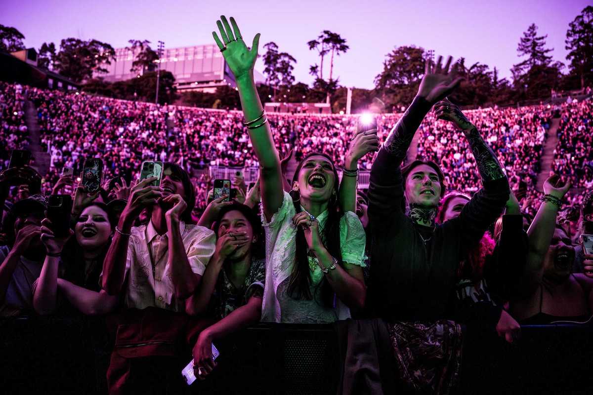 a crowd of outdoor concert goers bathed in pink light
