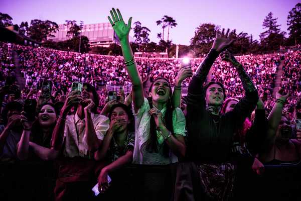 a crowd of outdoor concert goers bathed in pink light