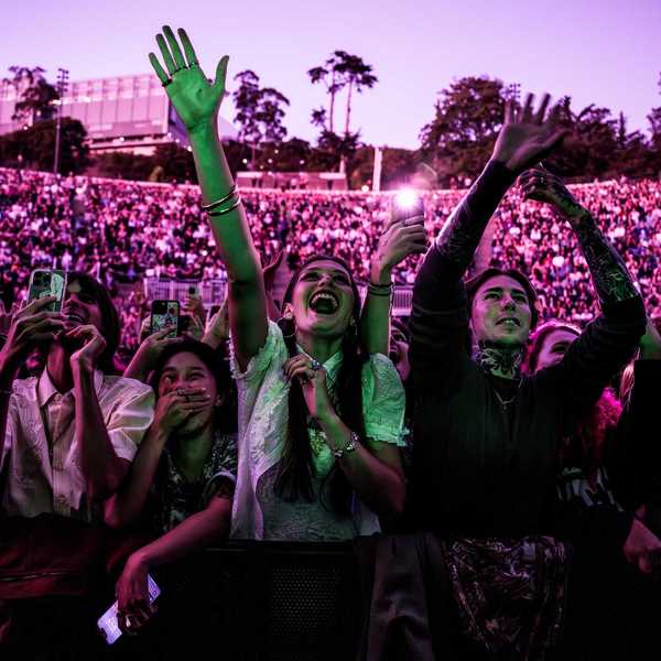 a crowd of outdoor concert goers bathed in pink light