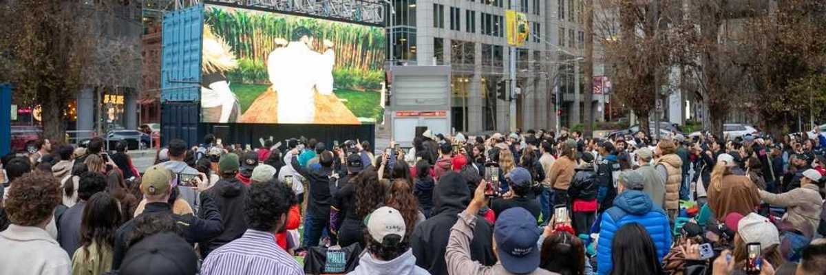 a crowd of peole watching a large screen in an urban area