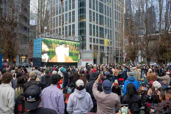 a crowd of peole watching a large screen in an urban area