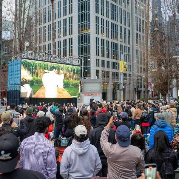 a crowd of peole watching a large screen in an urban area