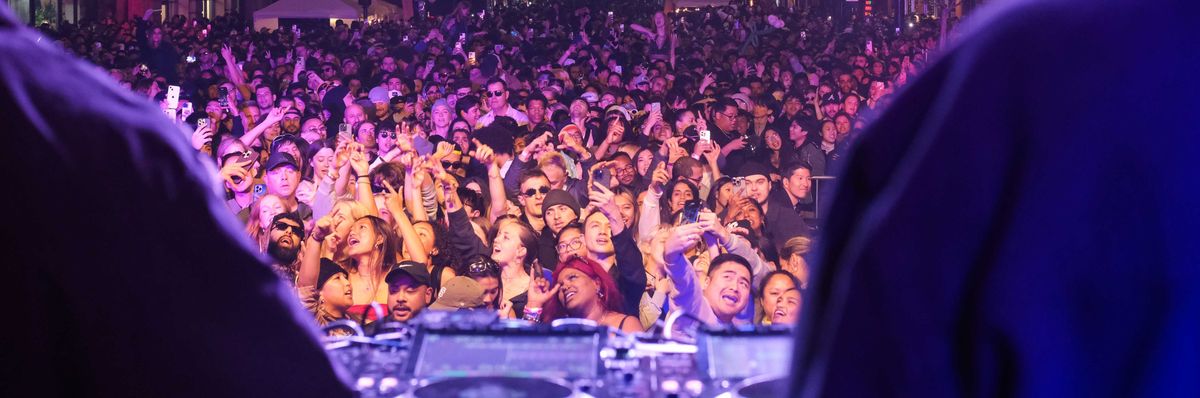 a crowd of people dancing in front of a dj booth outdoors