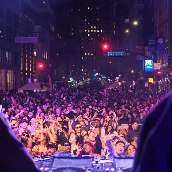 a crowd of people dancing in front of a dj booth outdoors
