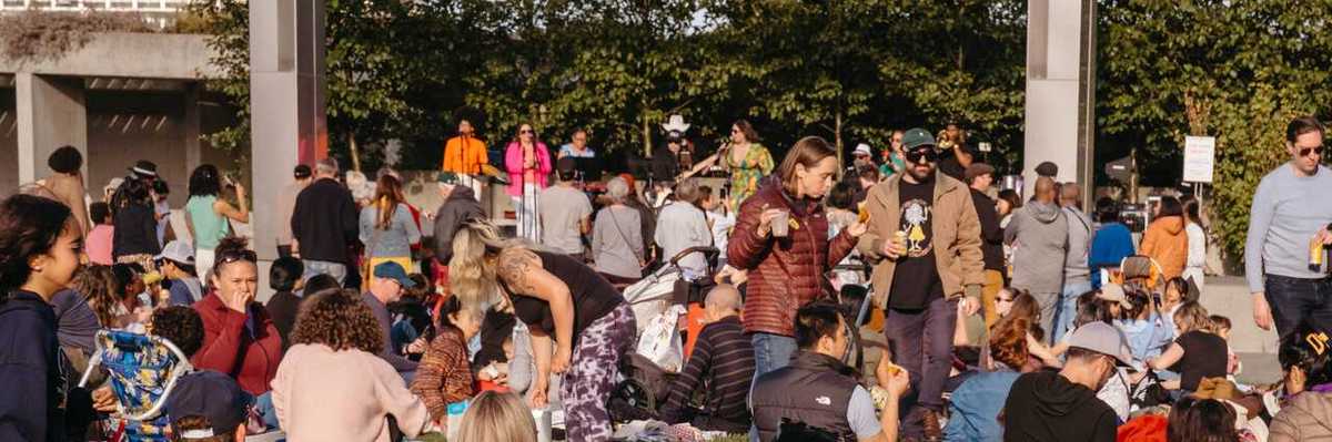 a crowd of people eating and drinking on a lawn in front of a stage