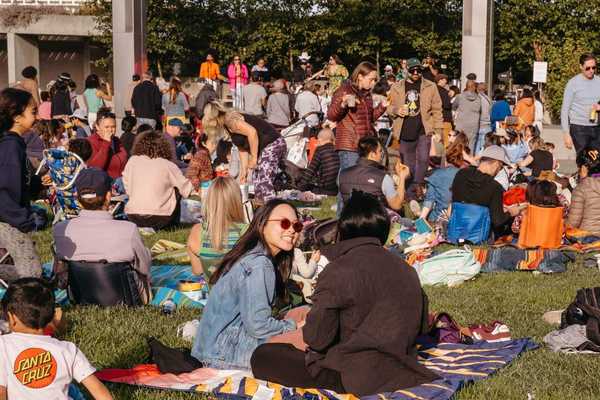 a crowd of people eating and drinking on a lawn in front of a stage