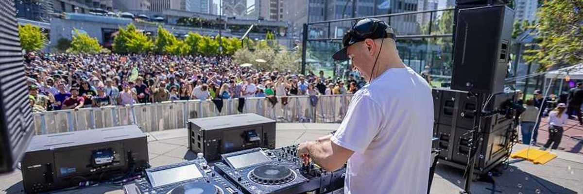 a dj on a stage in the middle of downtown SF with a large crowd in front