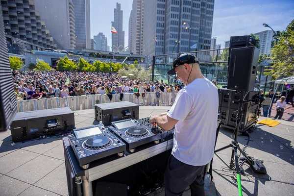 a dj on a stage in the middle of downtown SF with a large crowd in front
