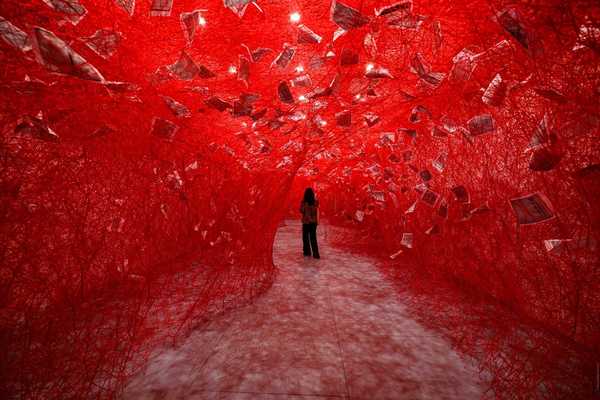 a figure standing in a tunnel of red woven yarn with pieces of paper suspended in it