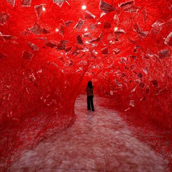 a figure standing in a tunnel of red woven yarn with pieces of paper suspended in it