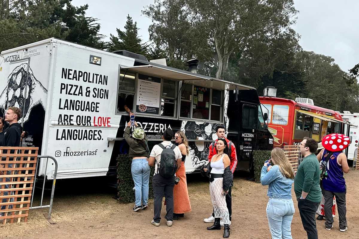 a food truck with a sign for neapolitan pizza and sign language with a line of people waiting to order