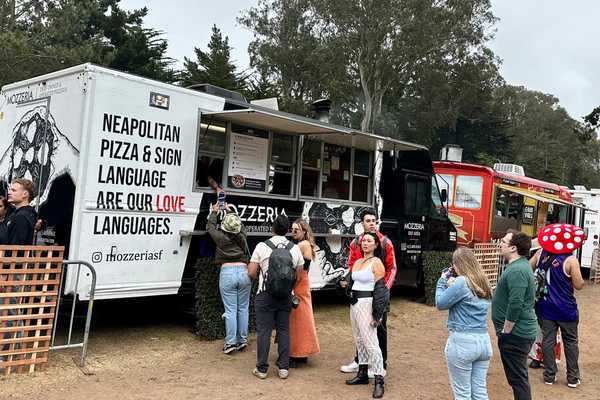a food truck with a sign for neapolitan pizza and sign language with a line of people waiting to order