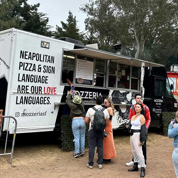 a food truck with a sign for neapolitan pizza and sign language with a line of people waiting to order
