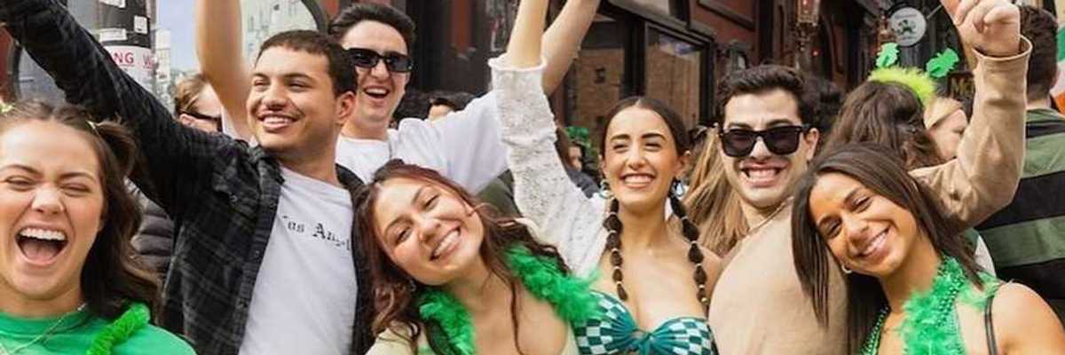 a group of young people wearing green and posing in front of an Irish pub