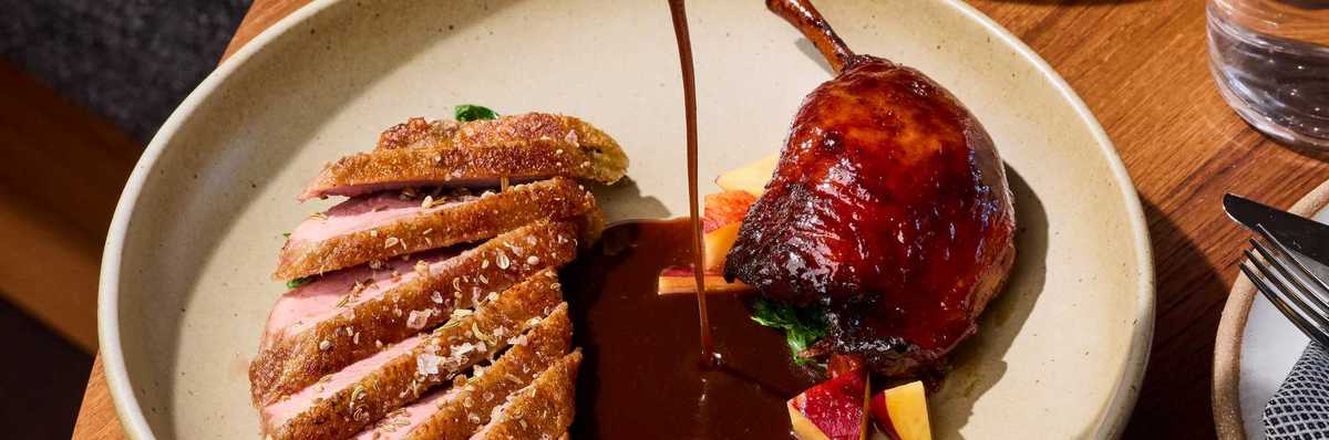 a hand pouring jus over a dish of duck breast