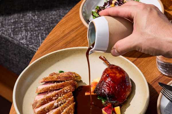a hand pouring jus over a dish of duck breast