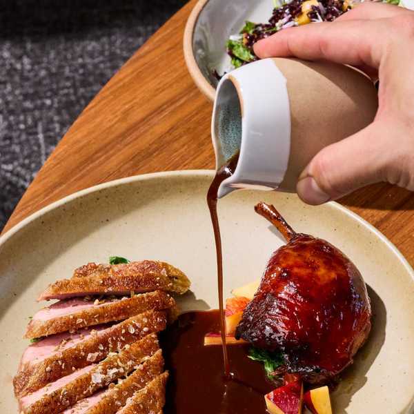 a hand pouring jus over a dish of duck breast