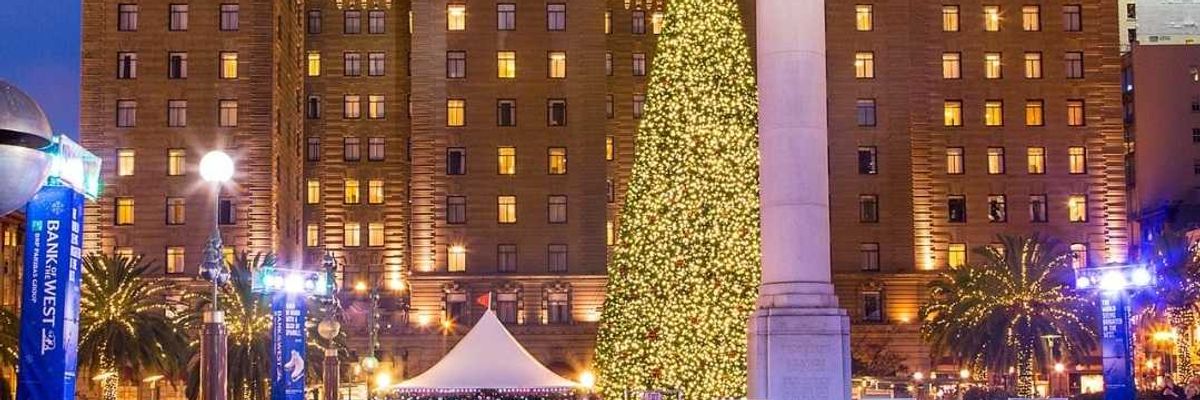 a holiday ice skating rink with a christmas tree and a large historic hotel lit up behind it