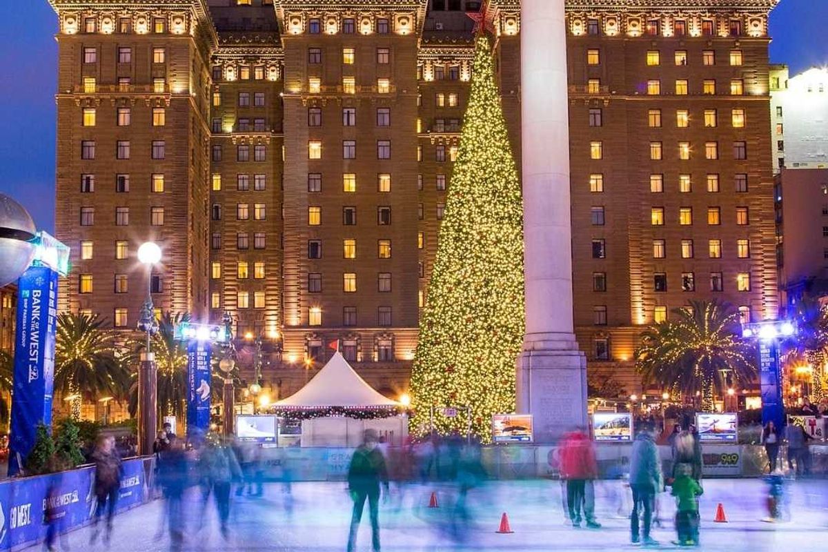 a holiday ice skating rink with a christmas tree and a large historic hotel lit up behind it
