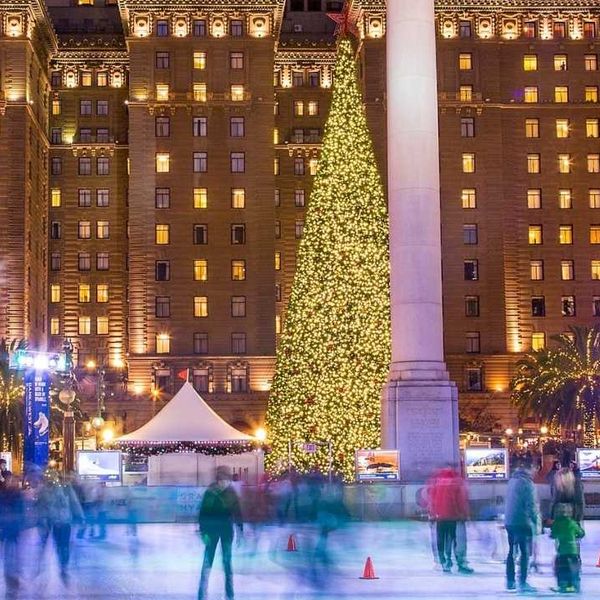a holiday ice skating rink with a christmas tree and a large historic hotel lit up behind it