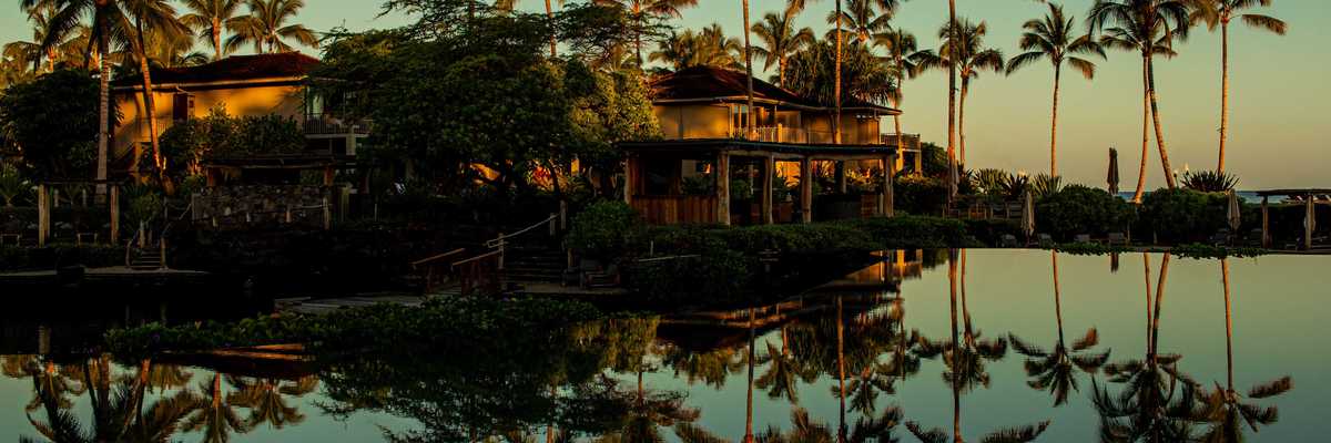 a hotel and palm trees reflected in a pool at sunset
