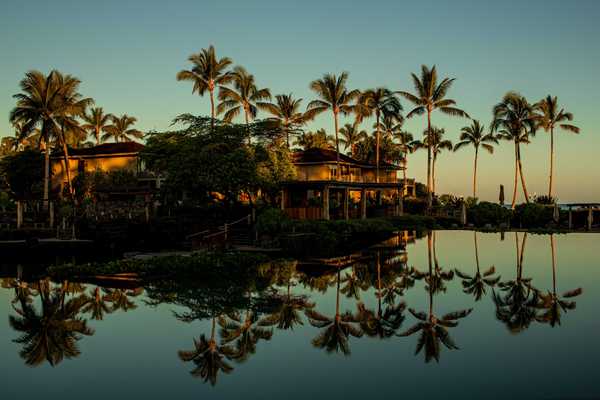 a hotel and palm trees reflected in a pool at sunset